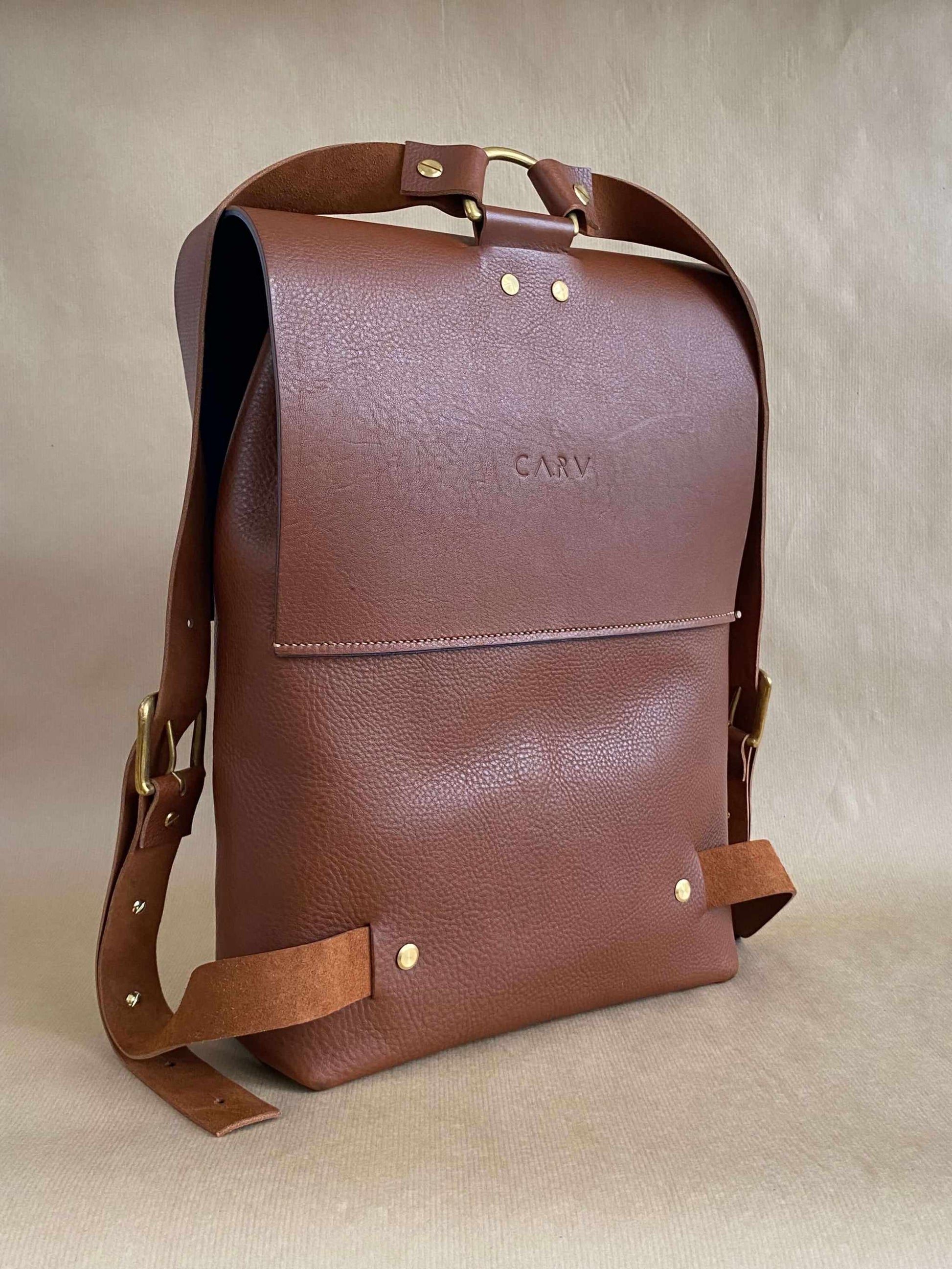 Tan leather backpack by CARV with a squared flap design and adjustable straps, showcasing minimalist style and craftsmanship.