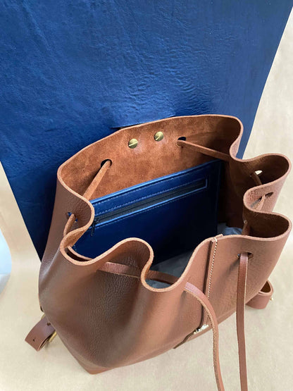 Open tan leather backpack with blue interior lining and magnetic clasp.