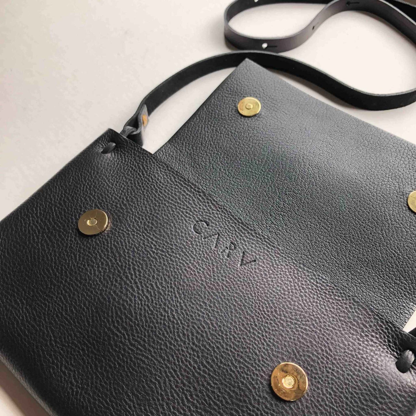 Fold Leather Crossbody Bag by CARV showing pebbled leather texture, black color, and brass buckle detailing.