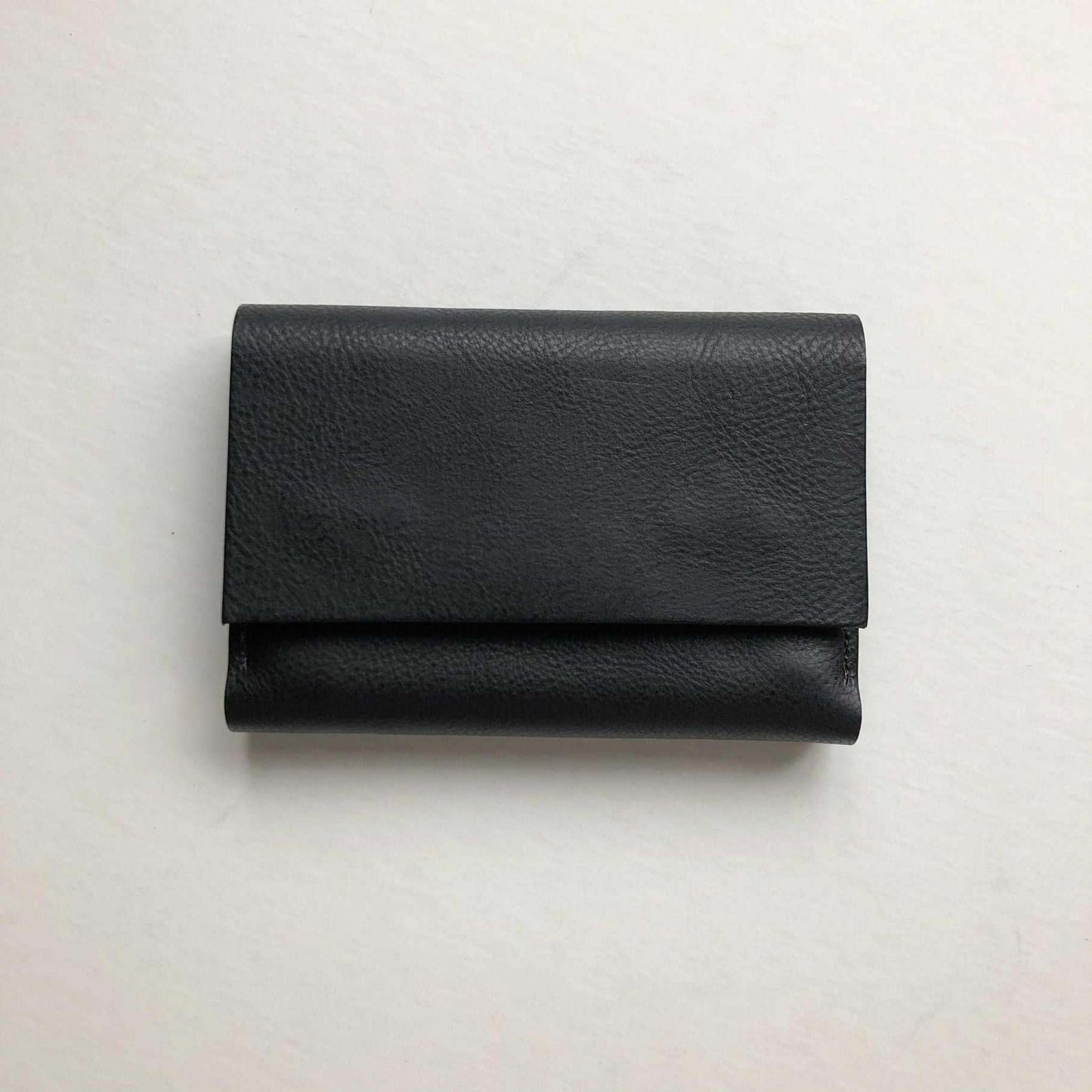 Small leather folding wallet purse, Knot Mini, in black, handcrafted from vegetable-tanned leather with hidden magnetic closures and spacious interior, on white background.