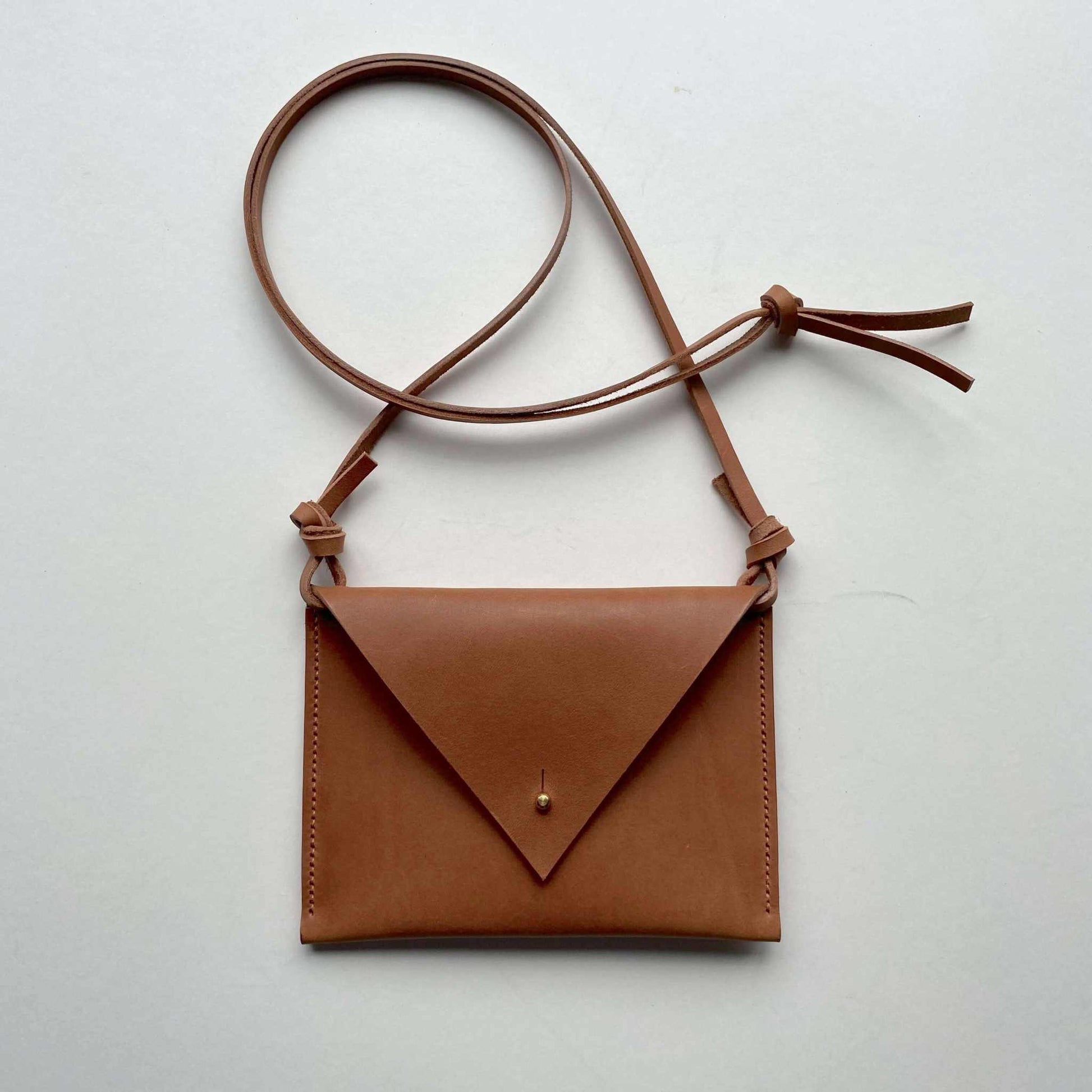 Cognac tan Drifter Mini Pocket Bag made from sustainable leather with triangular flap and brass press stud closure.