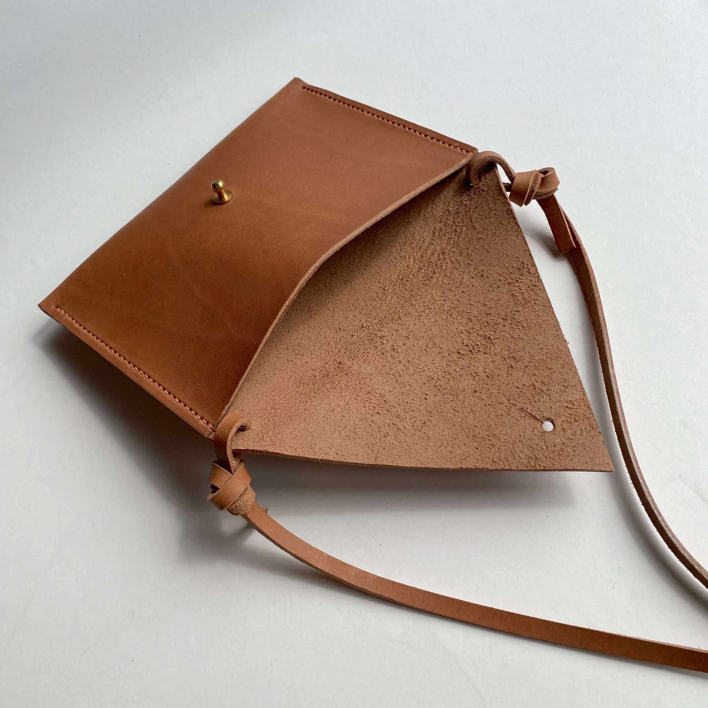 Minimalist Drifter Mini Pocket Bag in cognac tan leather with triangular flap and brass closure.