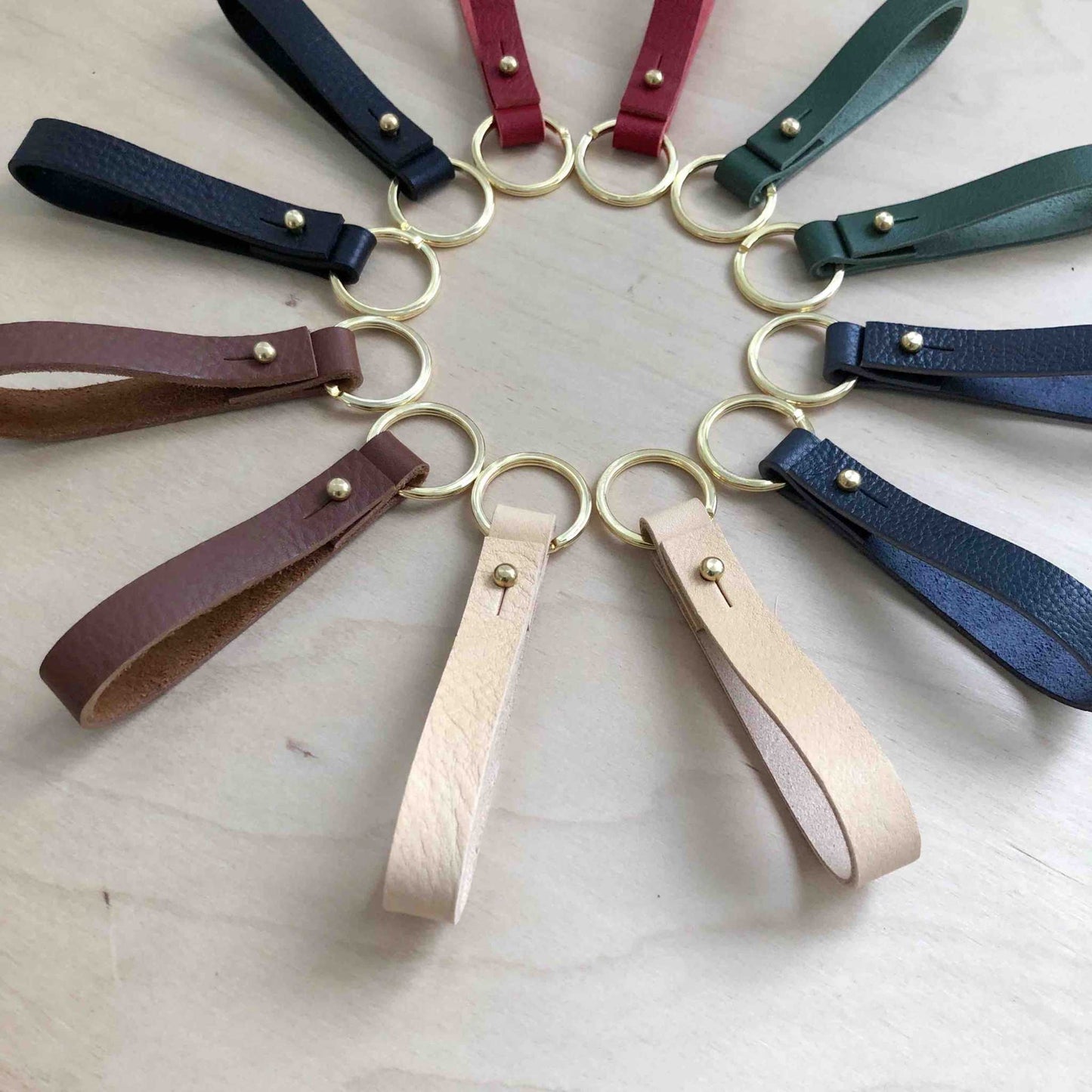 Personalised leather keyrings in black, brown, natural, red, and green with brass studs and rings.