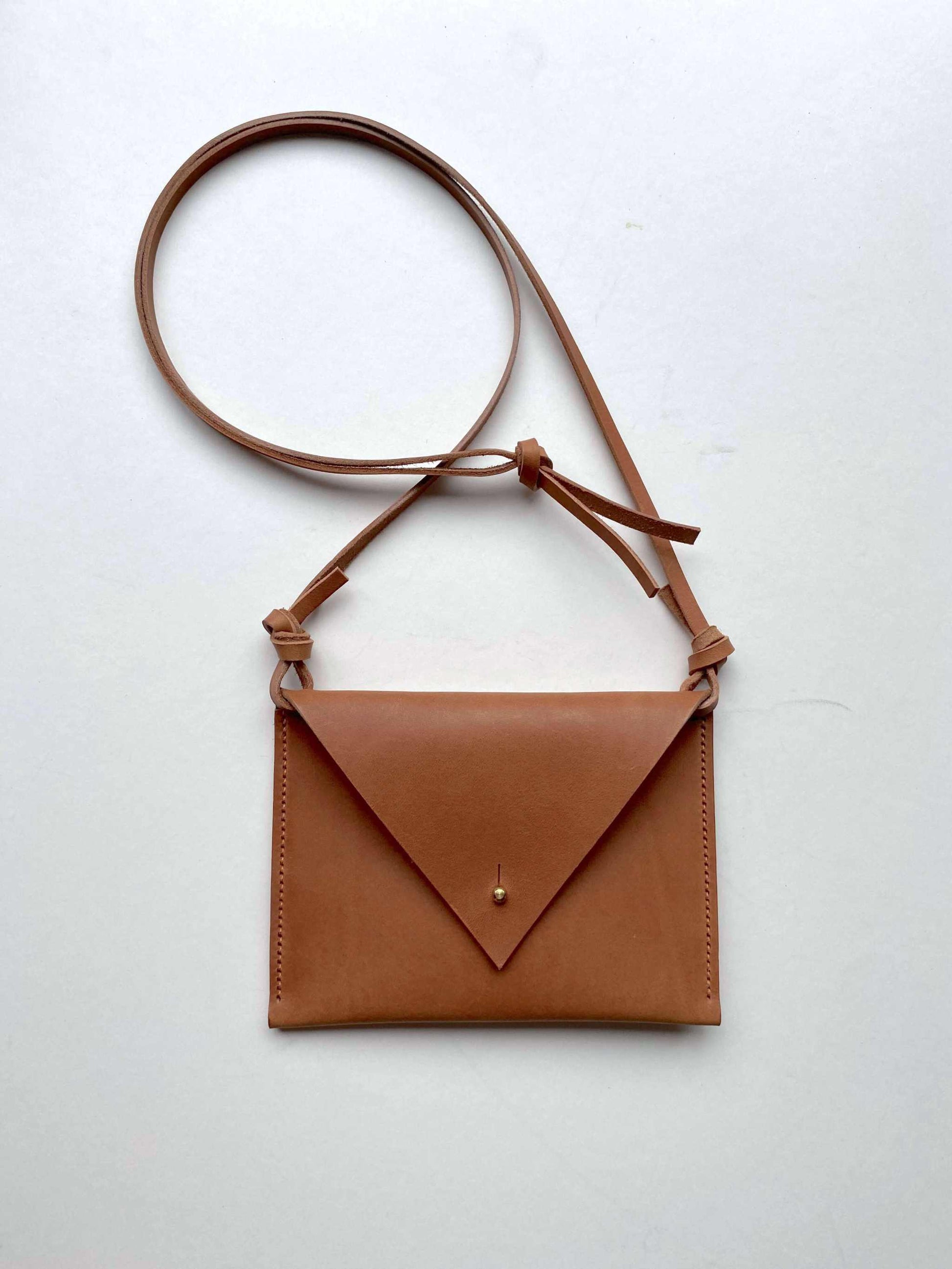 Drifter Mini Pocket Bag in cognac tan leather with triangular flap and brass closure.