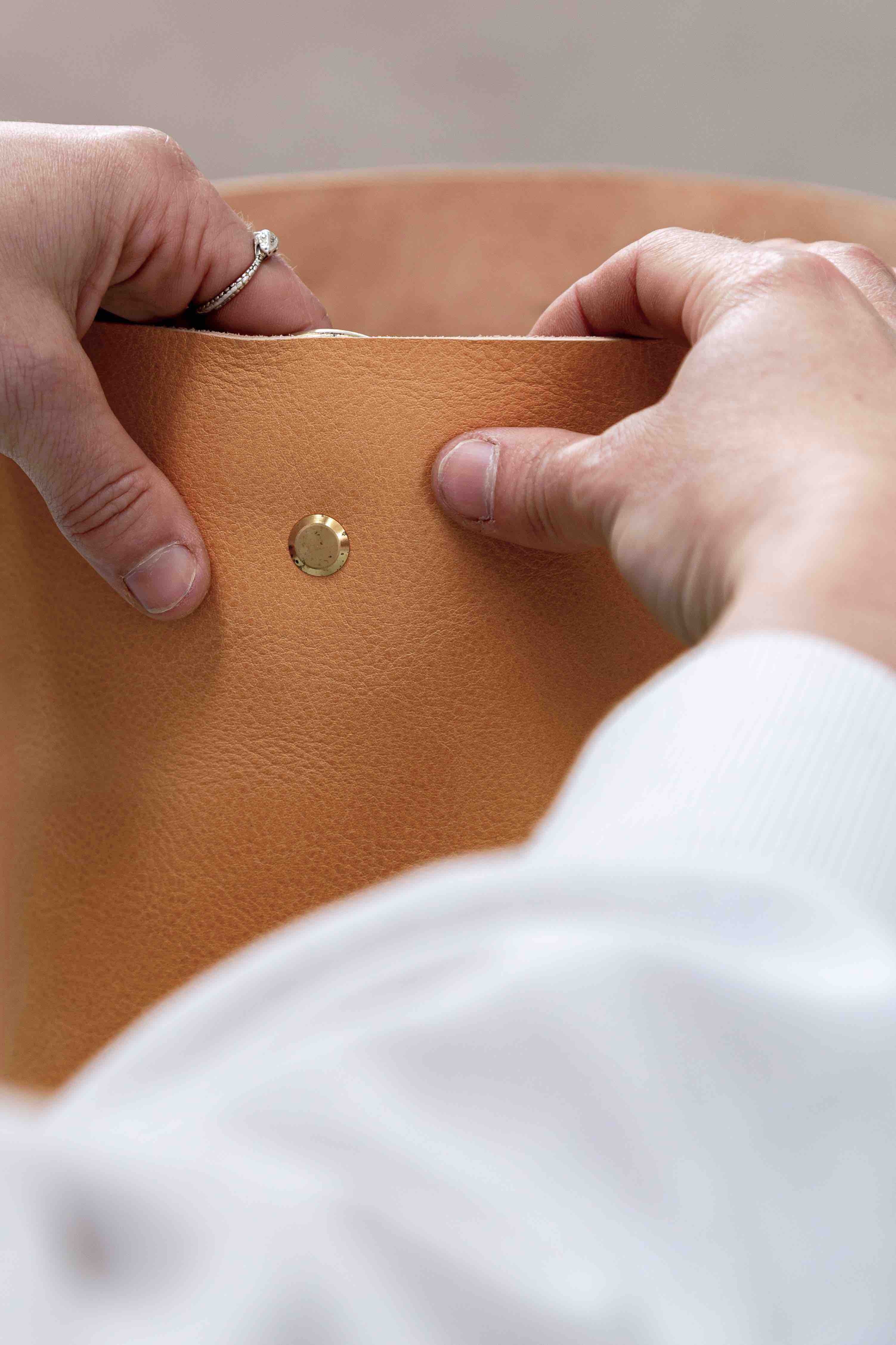 Hands adding solid brass hardware to a leather bag