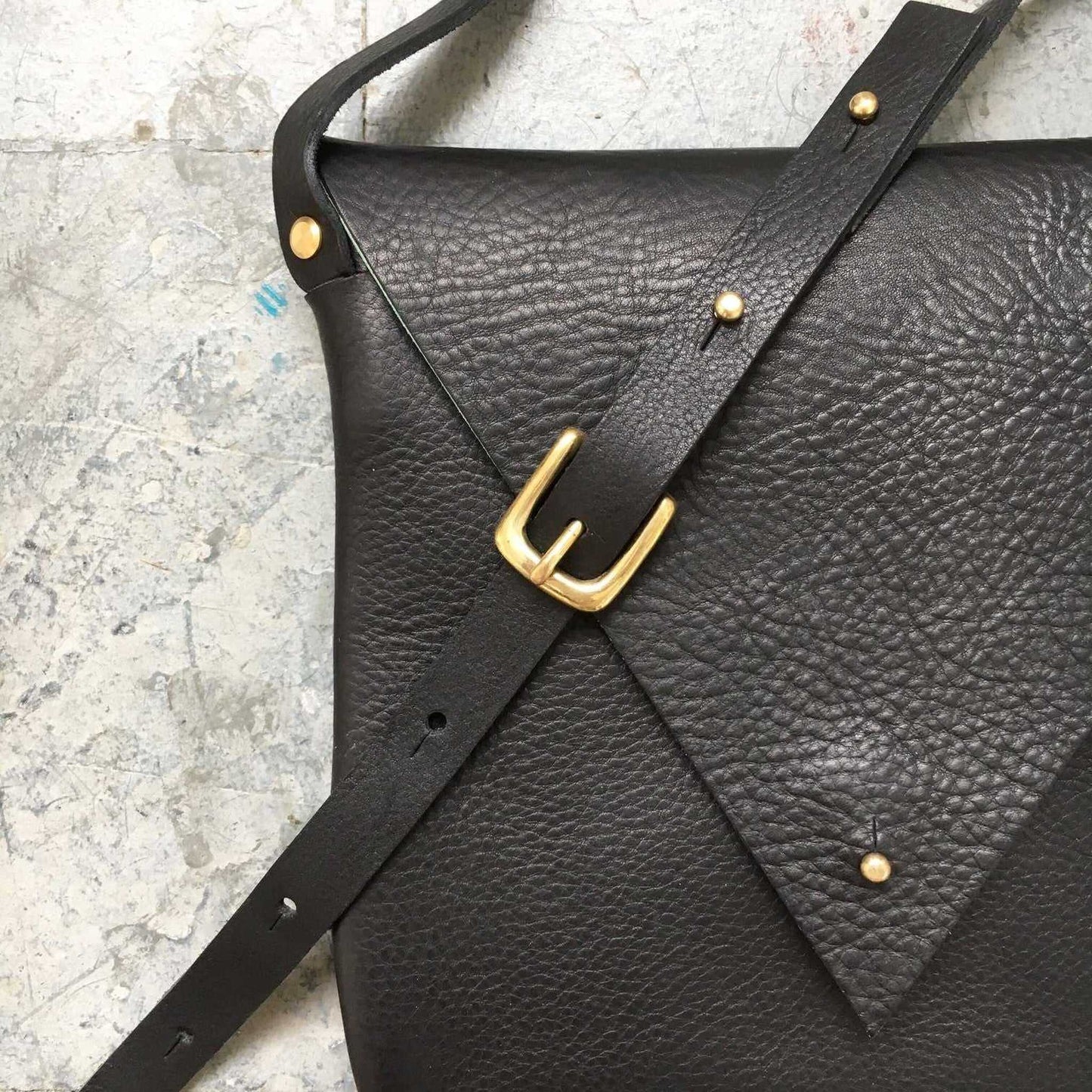 Drifter Leather Crossbody Bag in black with brass buckle and triangular flap design.