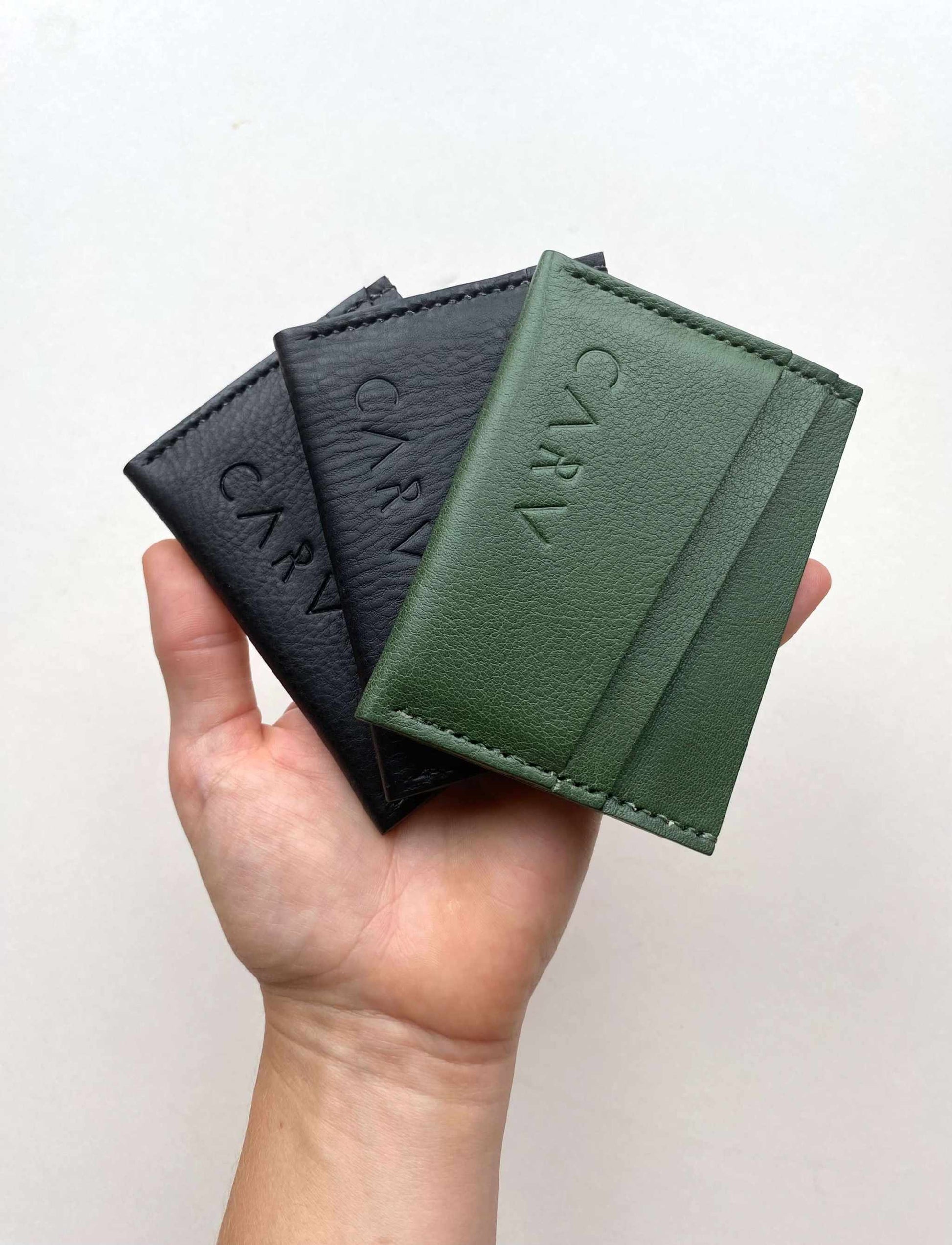 Green leather card holder by CARV in hand, showcasing the minimalist bifold design and eco-friendly craftsmanship.