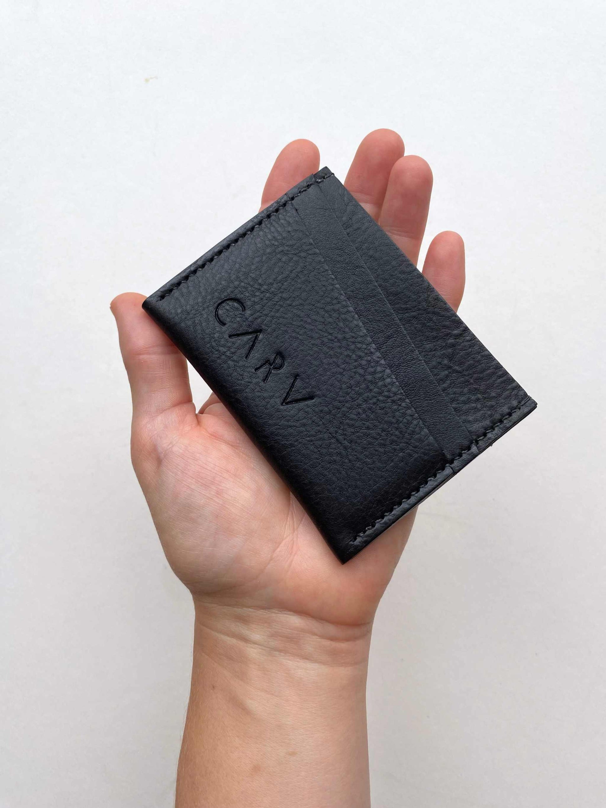 Hand holding a green leather card holder by CARV, showcasing minimalist bifold design and craftsmanship.