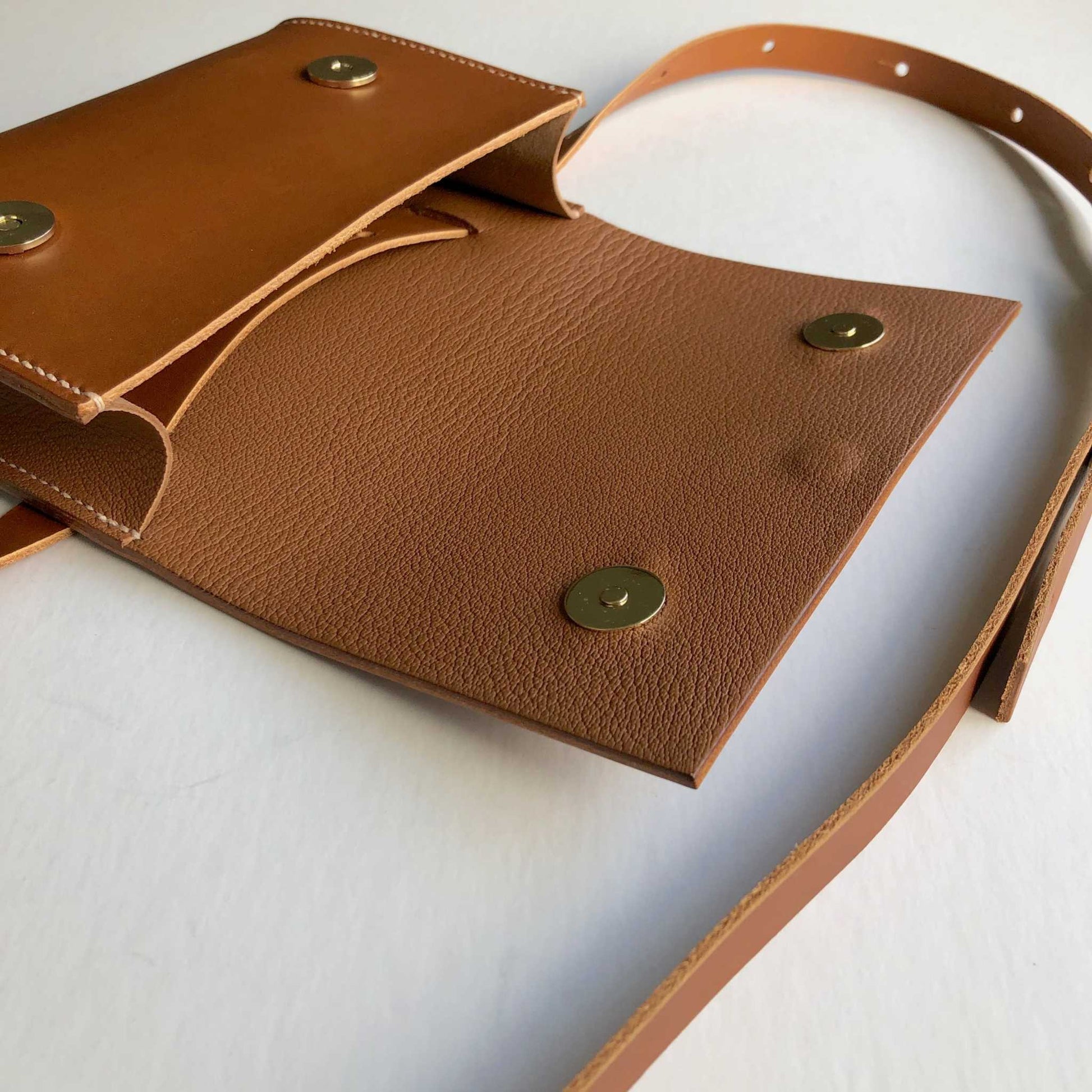 Tan Leather Belt Bag by CARV showing open flap with magnetic clasps and adjustable strap.