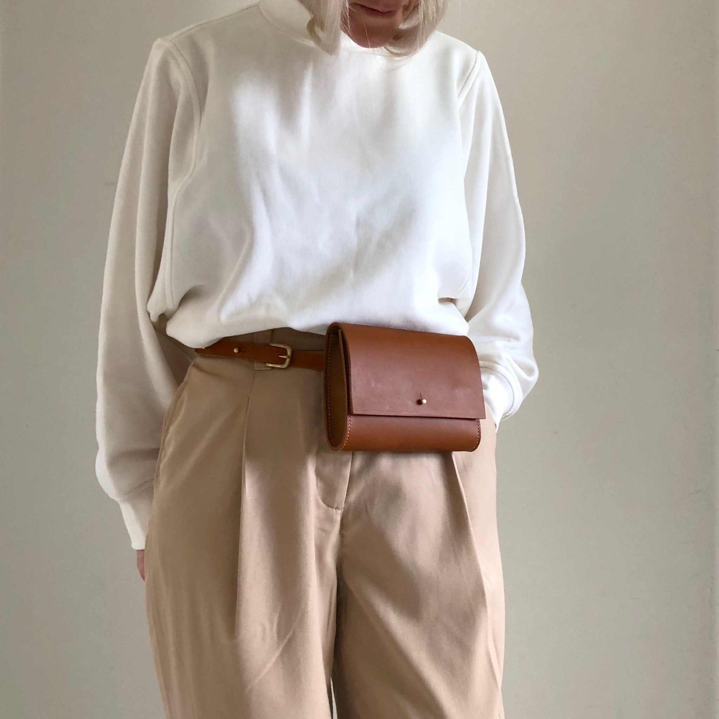 Sedna Tan Leather Belt Bag worn with a white top and beige pants, showcasing its minimalist design and craftsmanship.