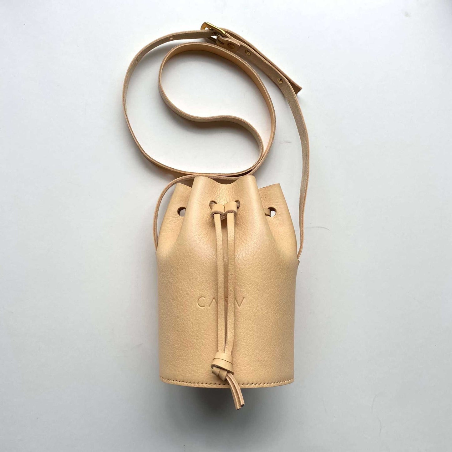 Beige Cylinder Mini Leather Bucket Bag with adjustable strap and brass hardware.