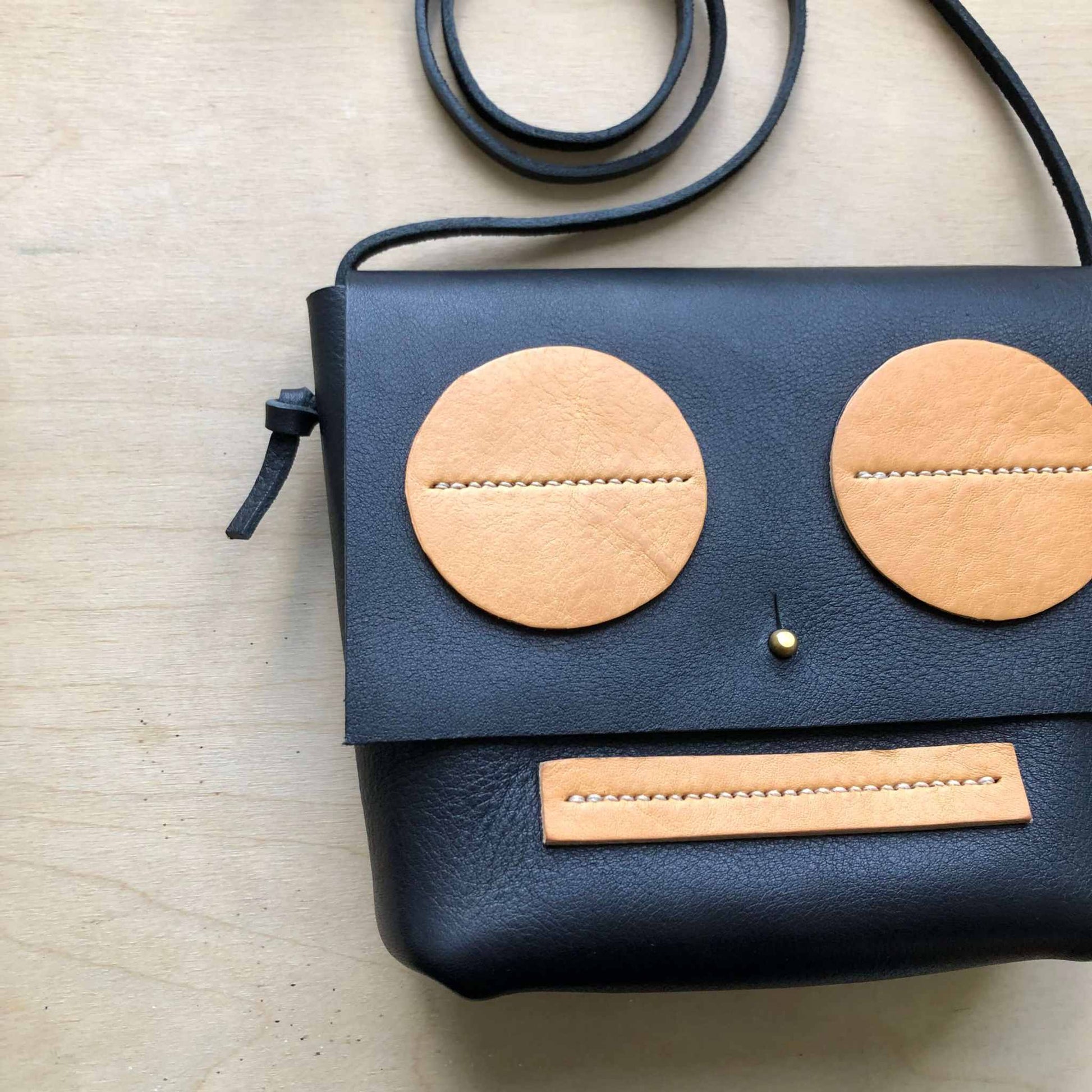 Little Robot Crossbody Bag in black leather with natural accents and adjustable strap.