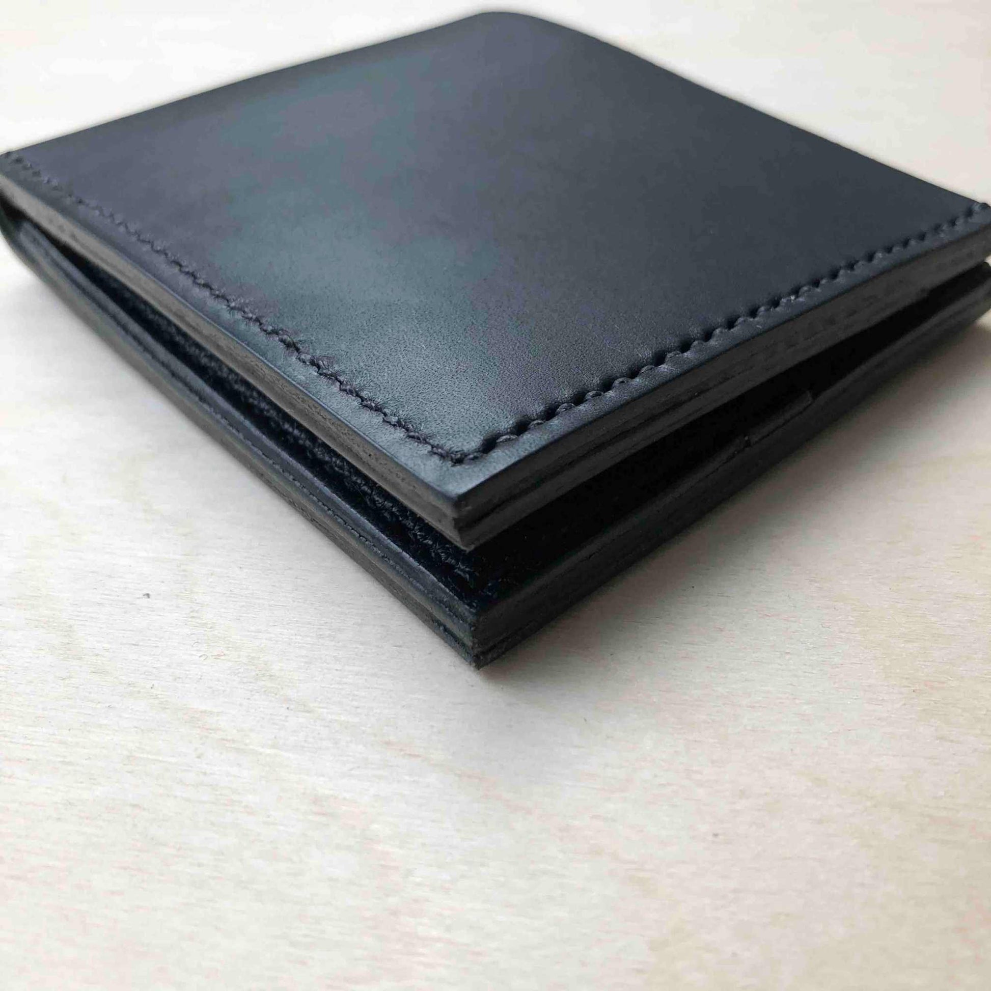 Handmade black leather bifold wallet with stitched edges on a wooden surface.