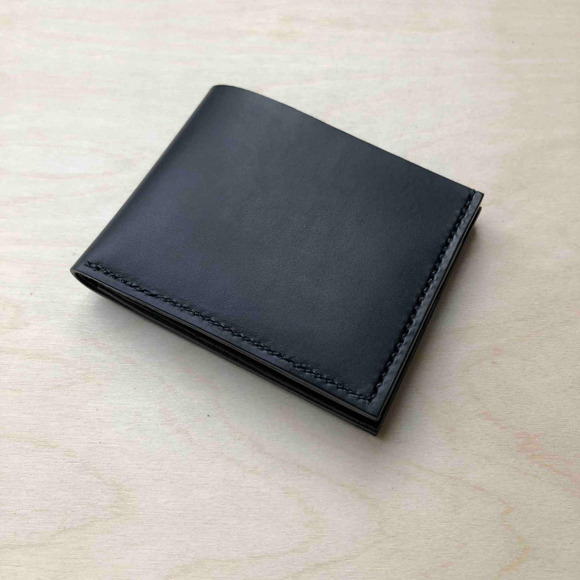 Handmade black leather bifold wallet crafted in England, showcasing minimalist elegance and sustainability.