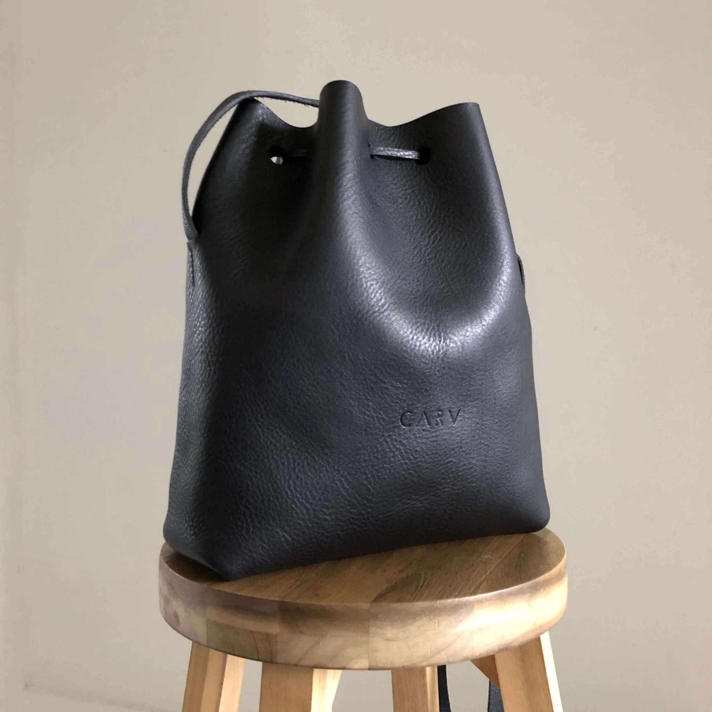 Nomad Maxi Leather Bucket Bag in black on wooden stool, handcrafted from vegetable-tanned leather.