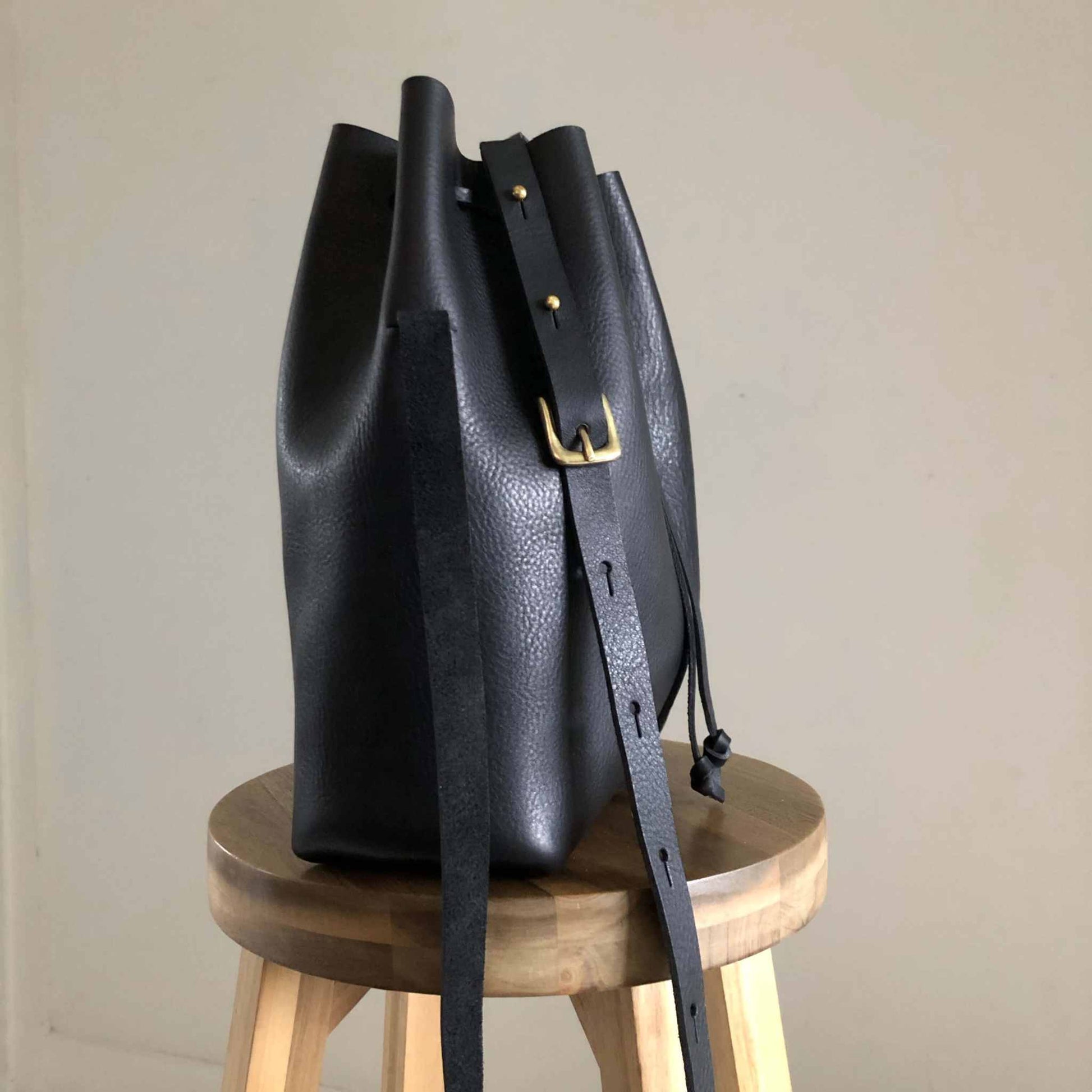 Nomad Maxi Leather Bucket Bag in black with adjustable strap on stool.