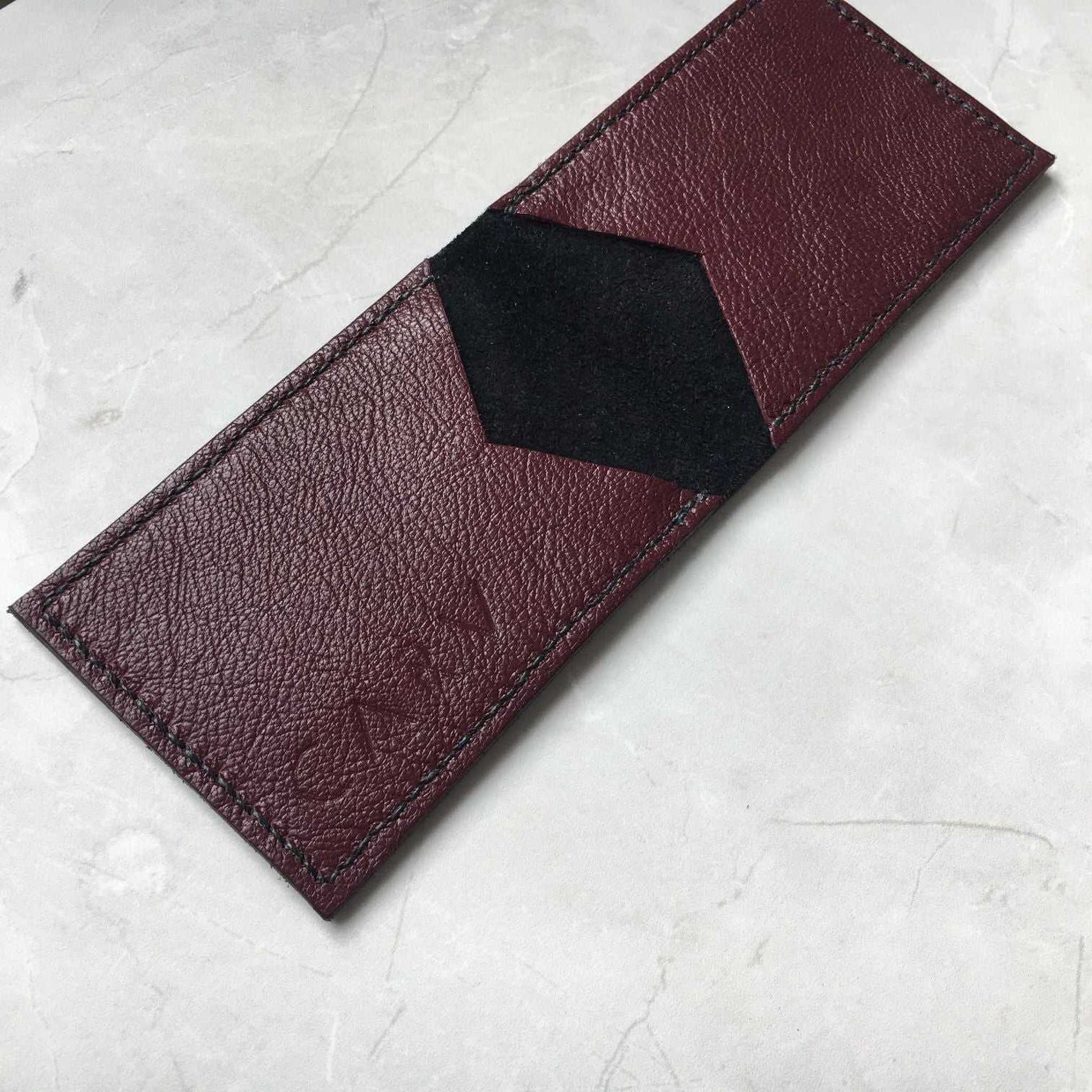 Nomad Leather Bifold Card Wallet in burgundy pebble leather on a marble surface.