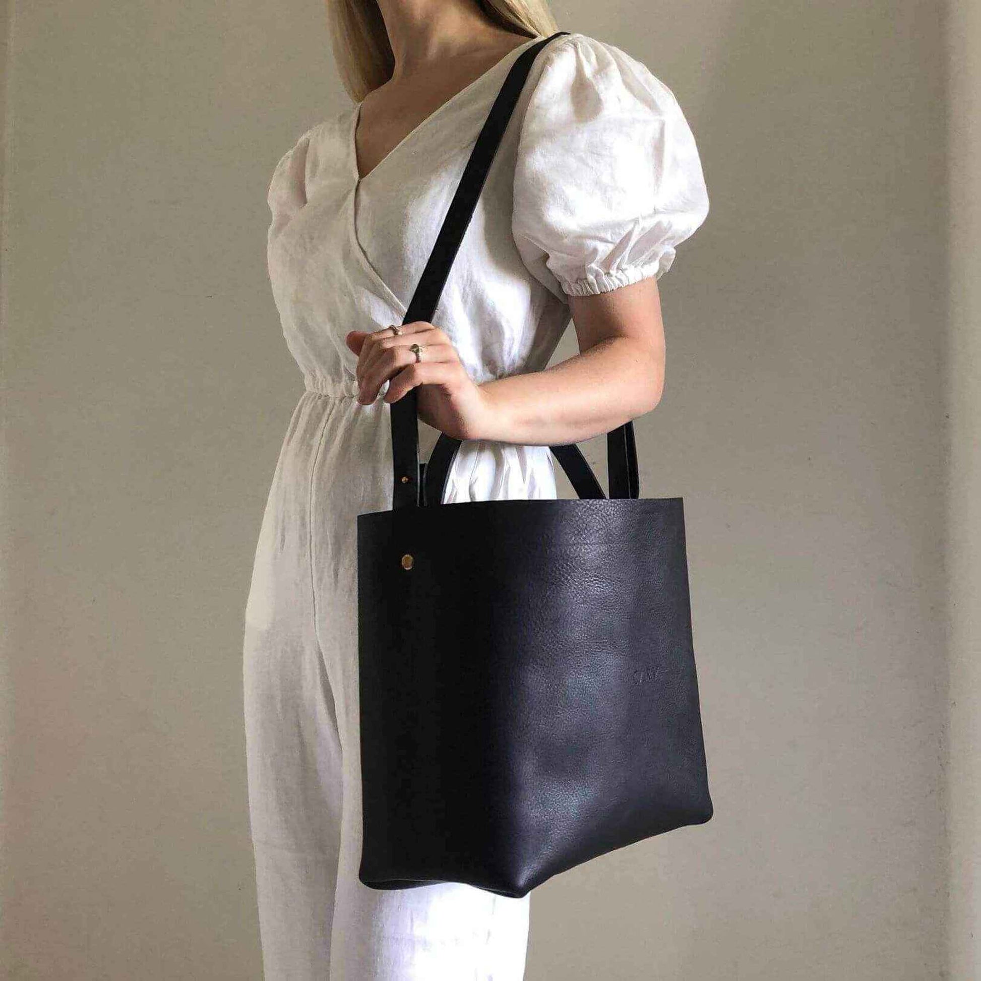 Basket Midi Leather Tote Bag in black, worn by a woman in a white dress, featuring versatile straps and minimalist design.