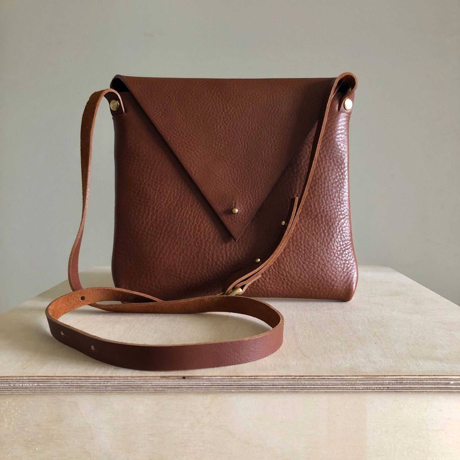 Drifter Leather Crossbody Bag in tan leather with triangular flap and adjustable strap.