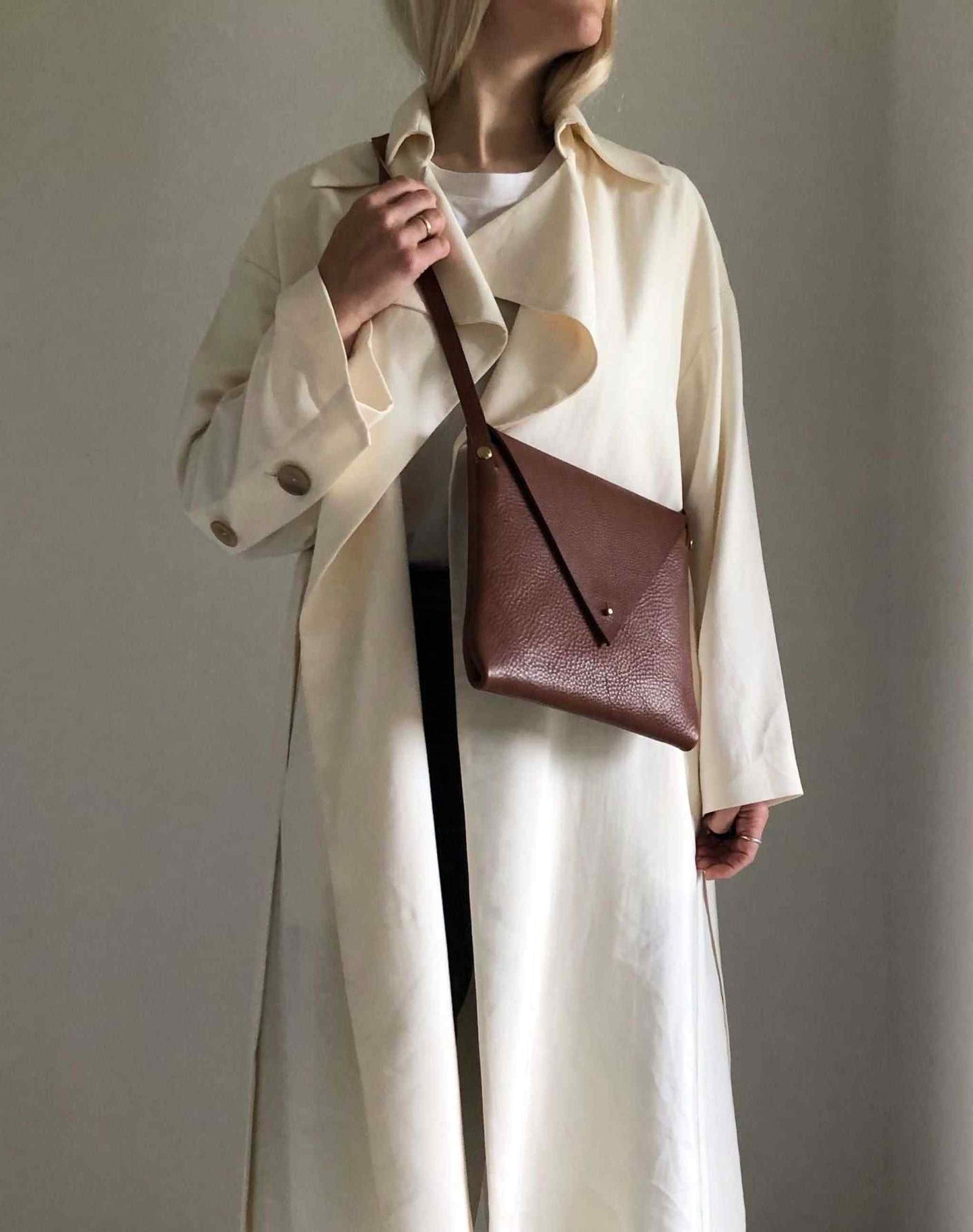 Person wearing a tan Drifter Leather Crossbody Bag with a long white coat.