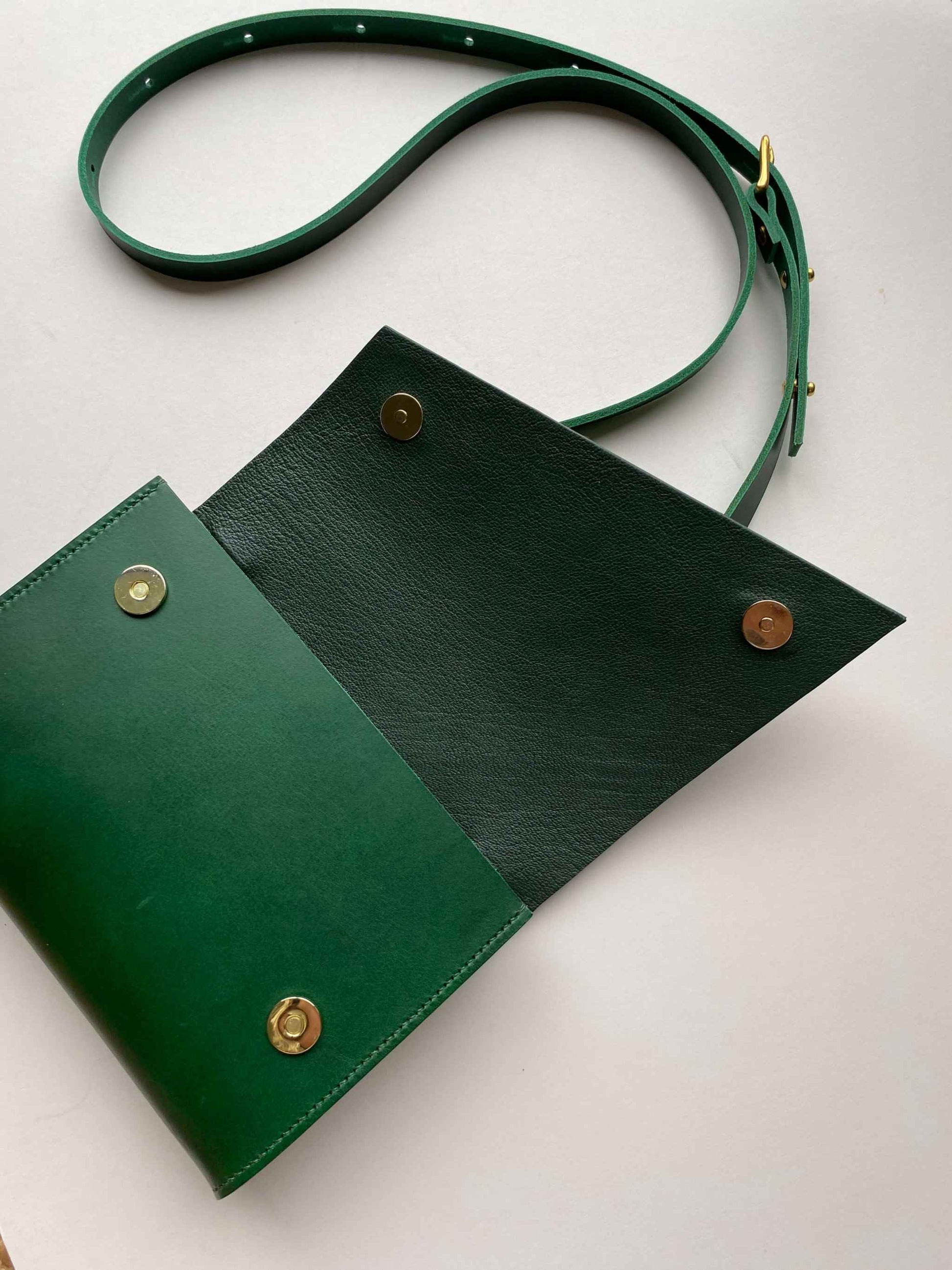 Green leather crossbody bag with adjustable strap and brass buckle.