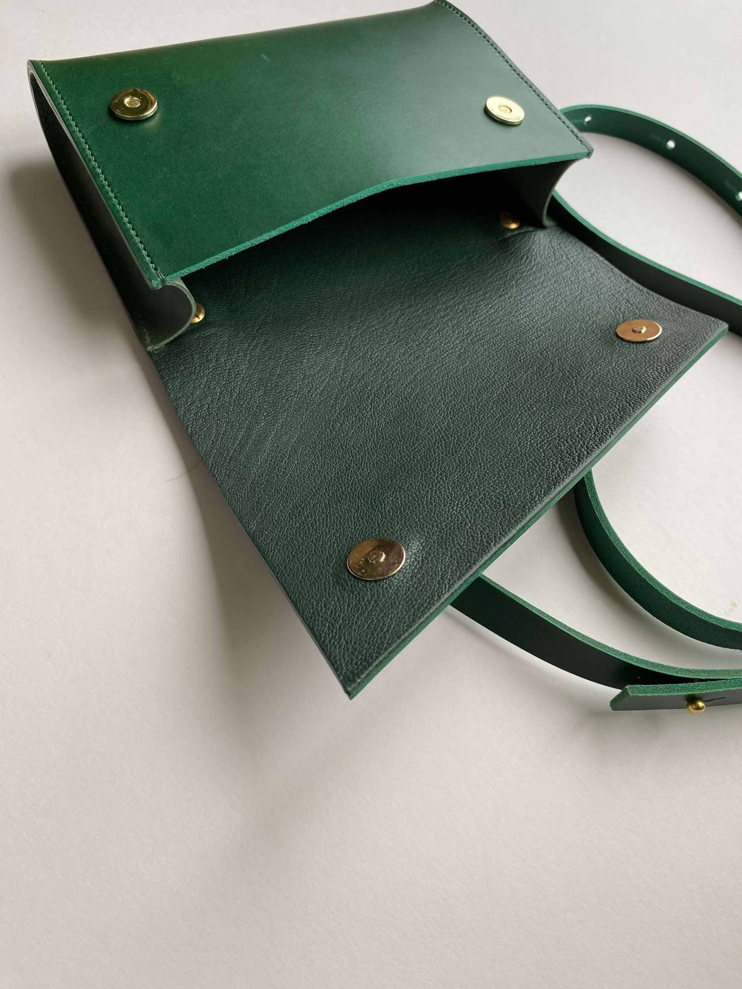 Mini green leather crossbody bag with adjustable strap and brass buckle, handcrafted from sustainable materials.