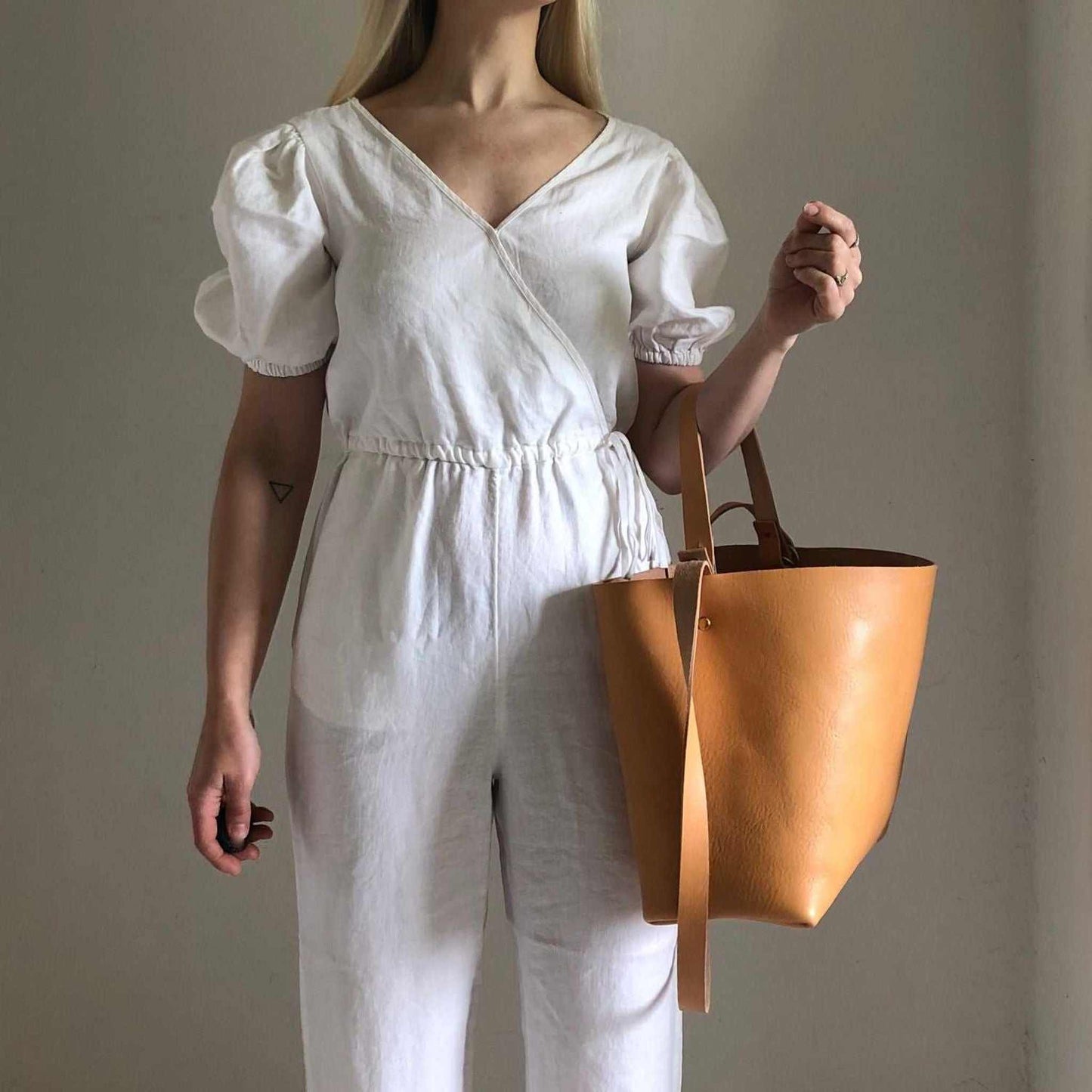 Basket Midi Leather Tote Bag in natural color, worn by a woman in a white jumpsuit, showcasing minimalist design and craftsmanship.