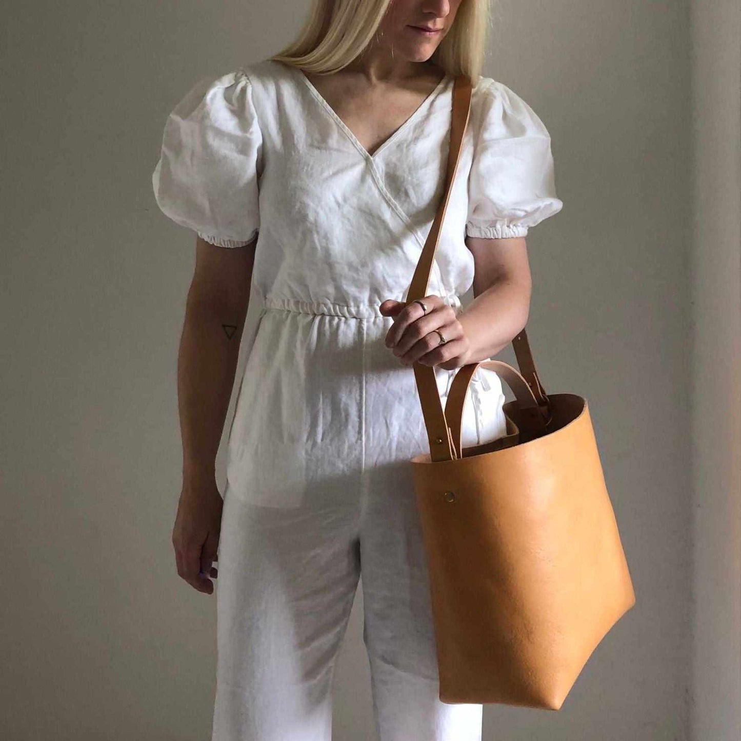 Basket Midi Leather Tote Bag in natural leather worn over shoulder by a woman in white outfit.