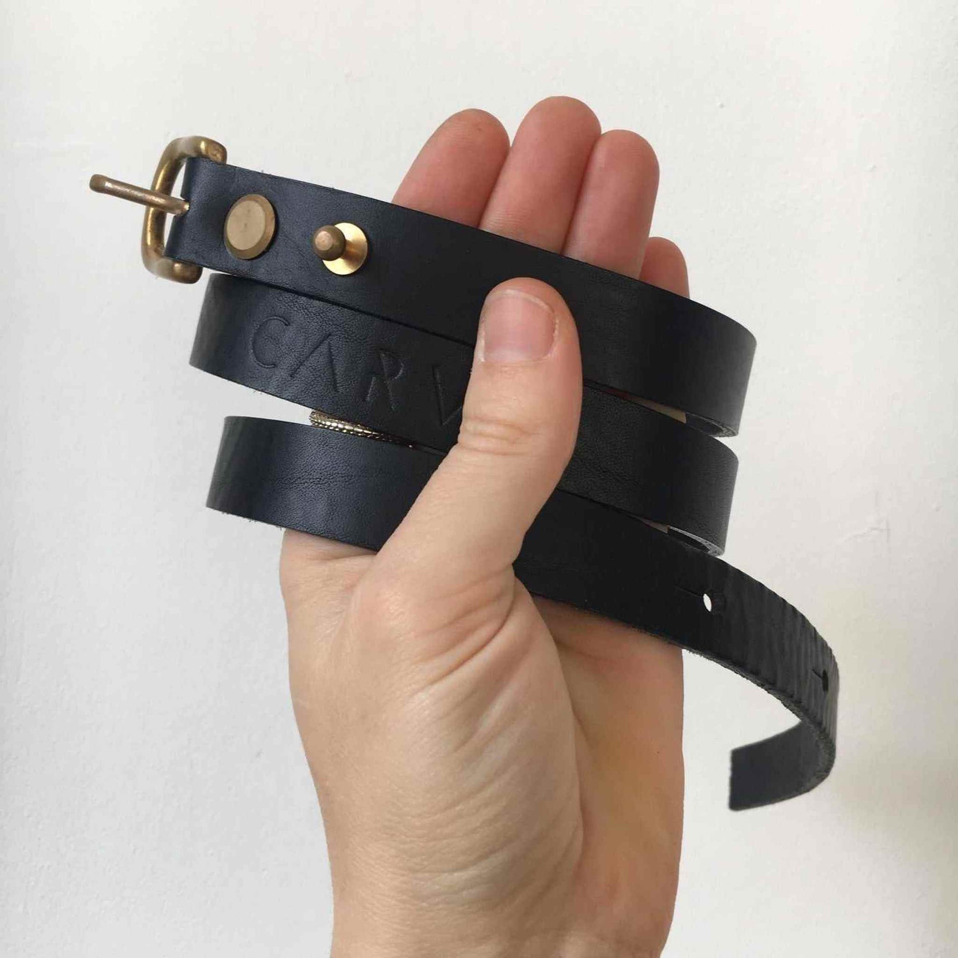 Handmade black leather belt with brass stud clasp, featuring skinny width and eco-friendly craftsmanship.