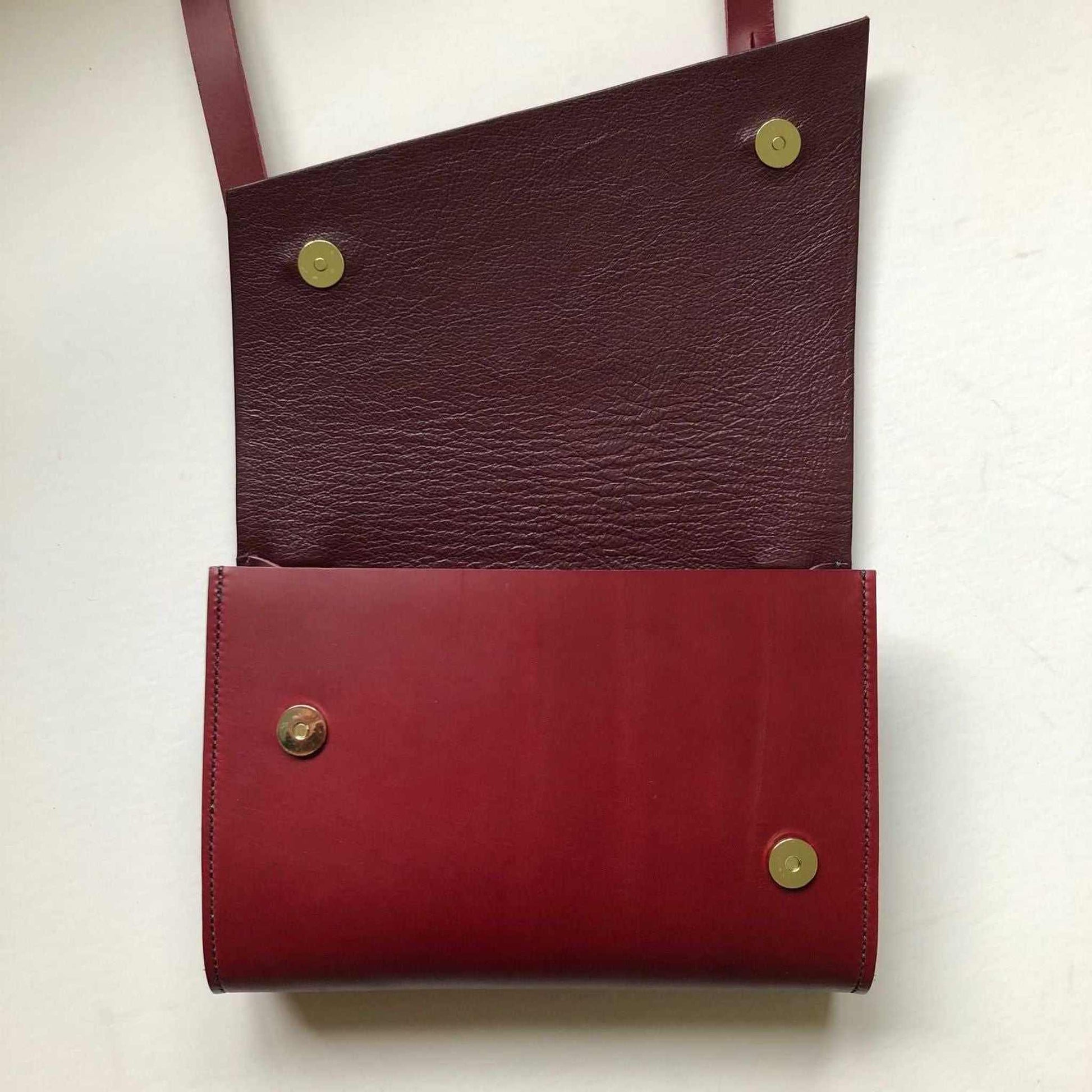 Red leather crossbody bag with asymmetrical flap and brass hardware.