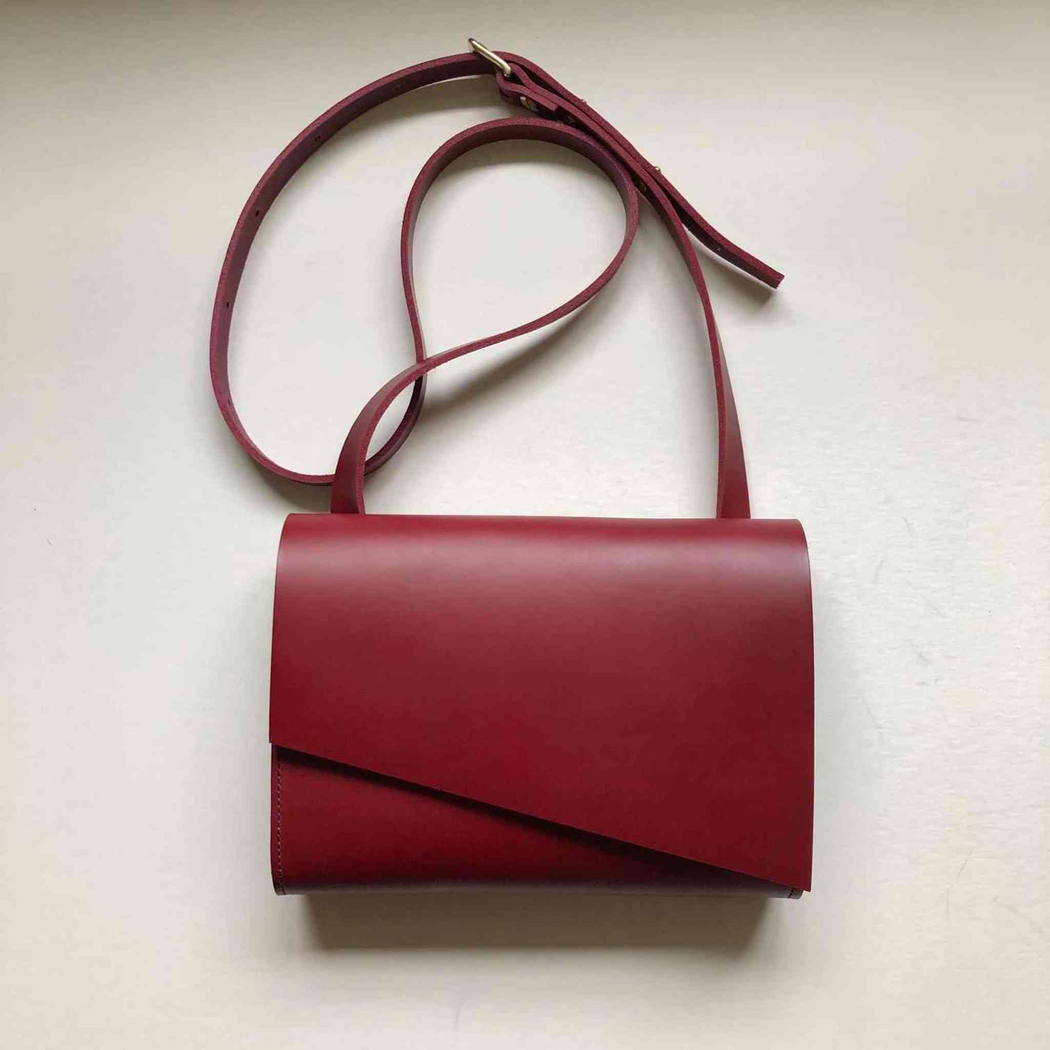 Red leather crossbody bag with adjustable strap and asymmetrical flap design.