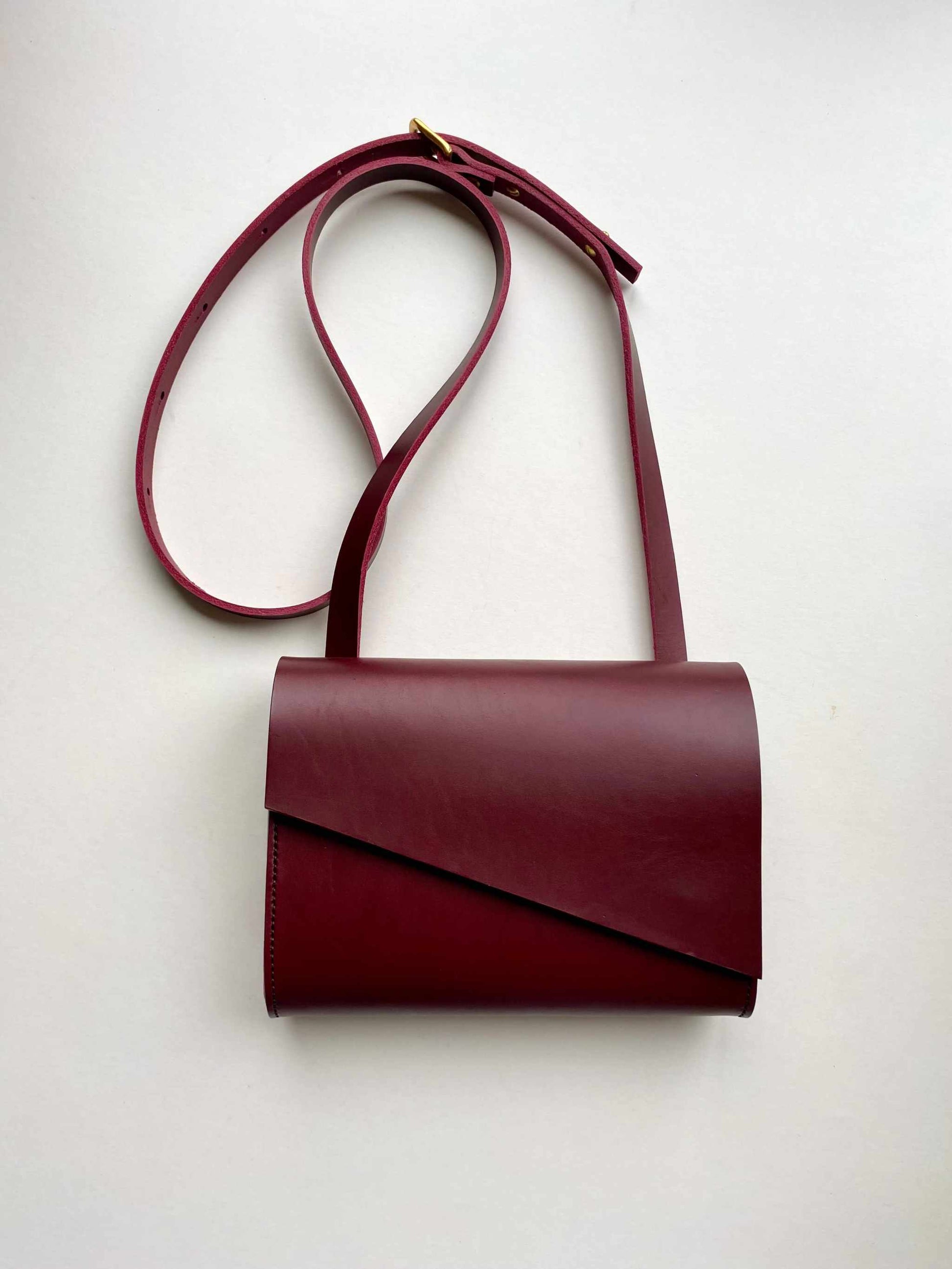 Mini red leather crossbody bag with adjustable strap and minimalist design.